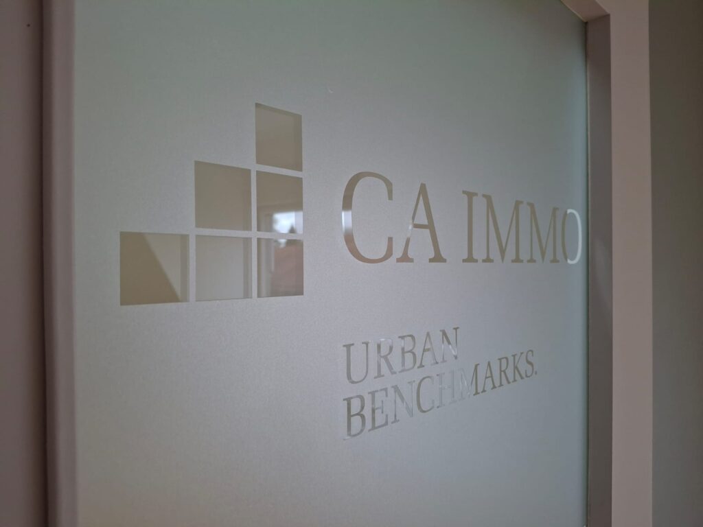 Milchglasfolie mit ausgespartem CA-Immo-Logo und Schriftzug „Urban Benchmarks.“ auf einer Glastür